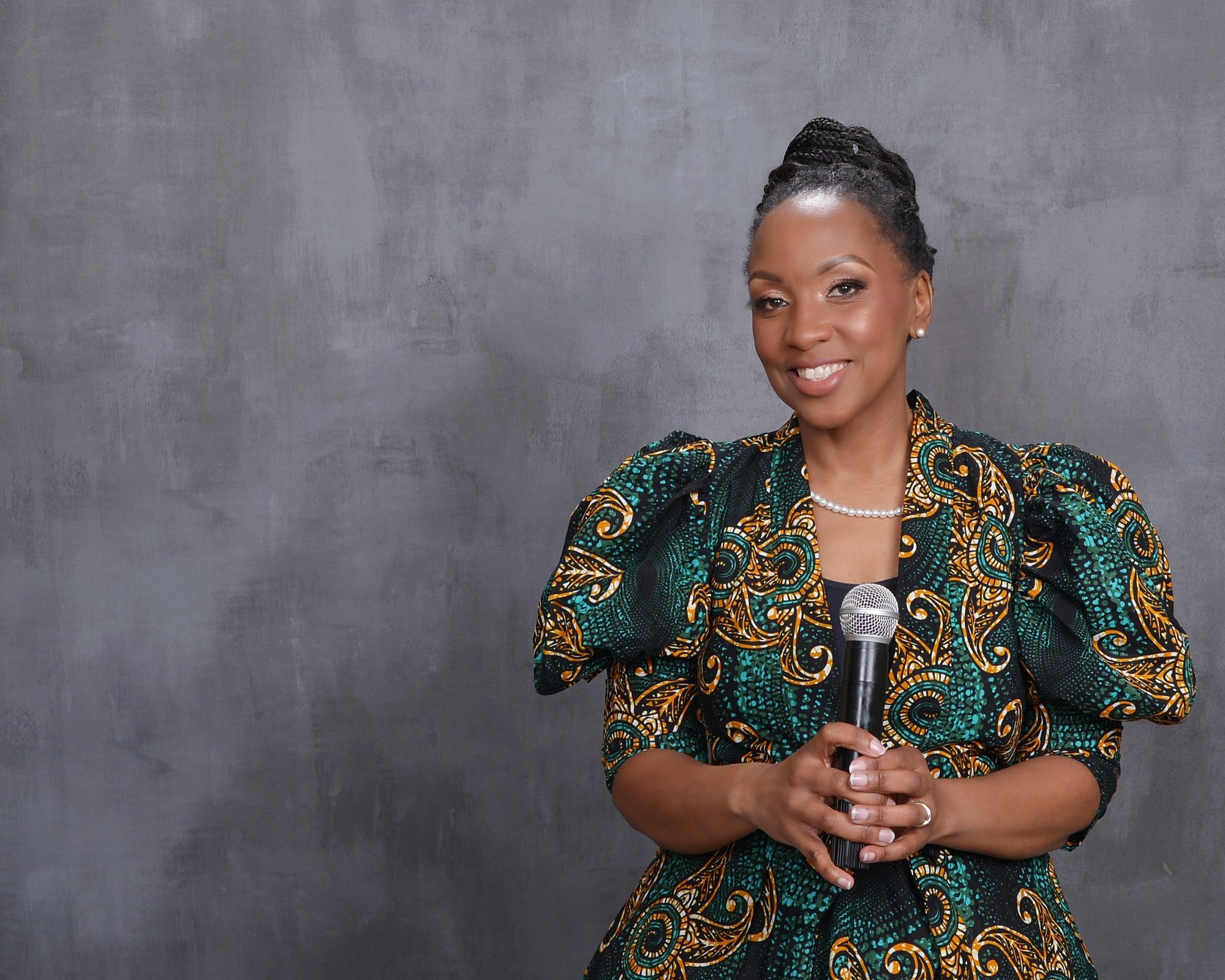 Eraina Ferguson smiling and holding a microphone, wearing a green and gold African print dress